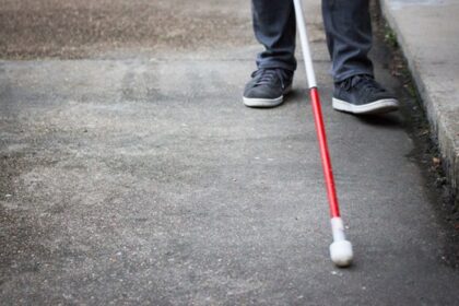 A person using a cane walks along a city street, showcasing mobility and independence