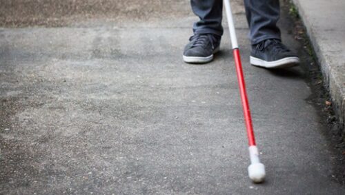 A person using a cane walks along a city street, showcasing mobility and independence