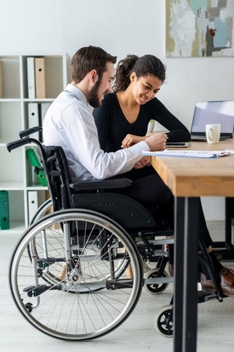 A man in a wheelchair and a woman are seated together at a table, engaged in conversation.