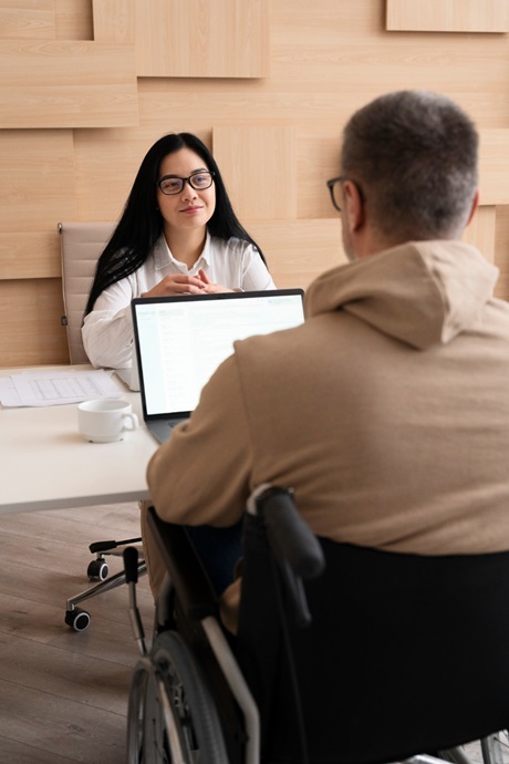 A man in a wheelchair sits at a table with a woman, both appearing to enjoy a discussion together.